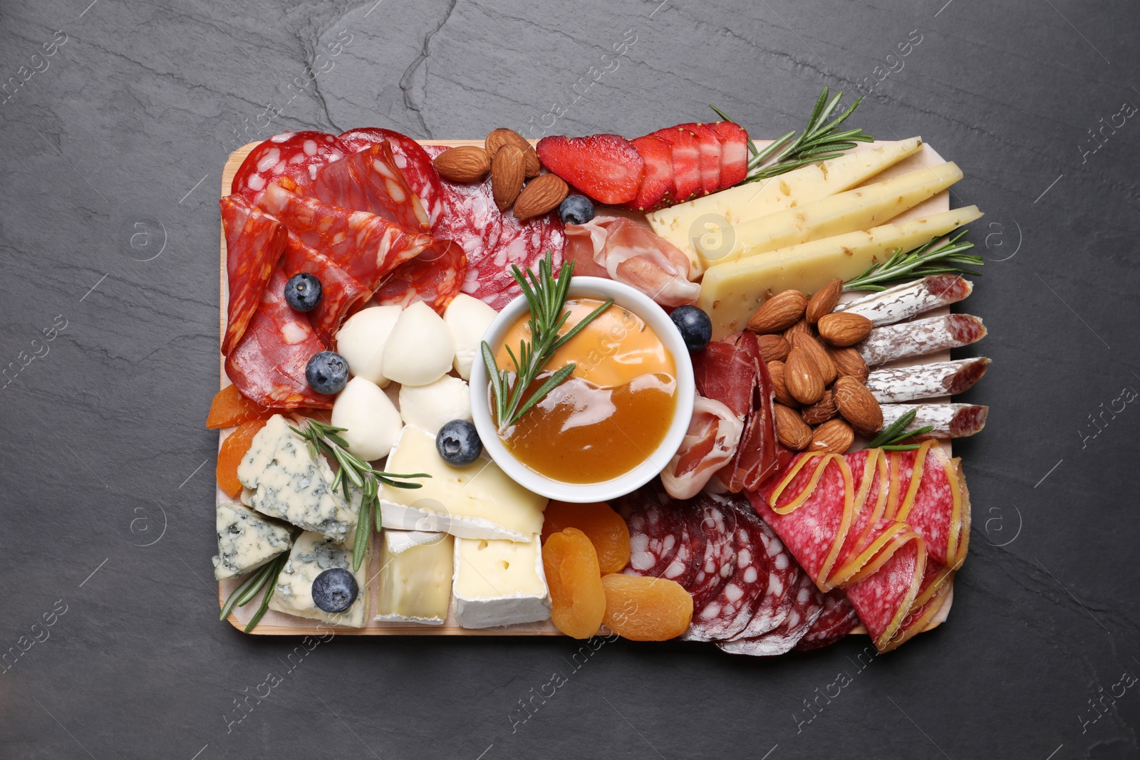 Photo of Wooden plate with different delicious snacks on black table, top view