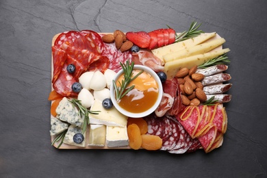 Photo of Wooden plate with different delicious snacks on black table, top view