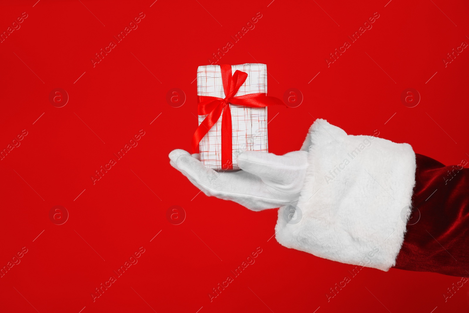 Photo of Santa Claus holding Christmas gift on red background, closeup of hand