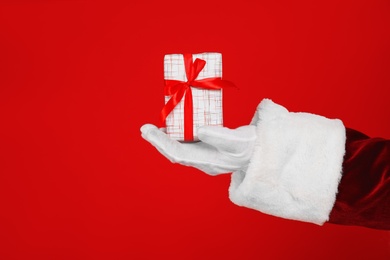 Photo of Santa Claus holding Christmas gift on red background, closeup of hand