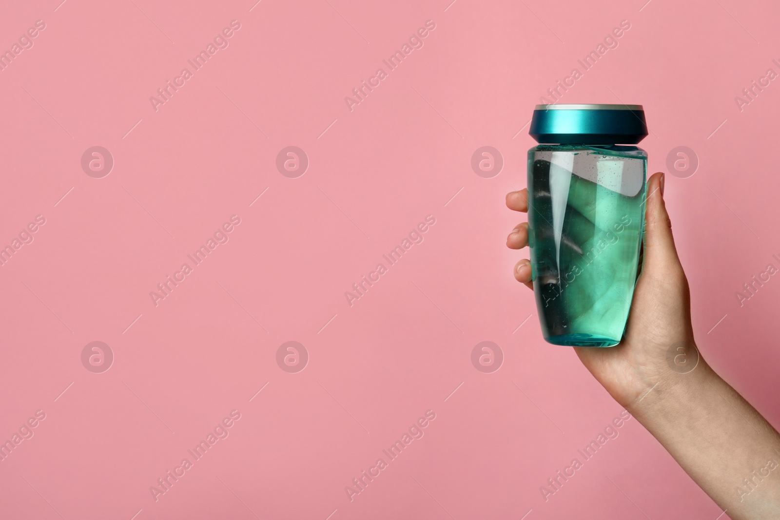 Photo of Woman holding bottle of hair care cosmetic product on pink background, closeup. Space for text