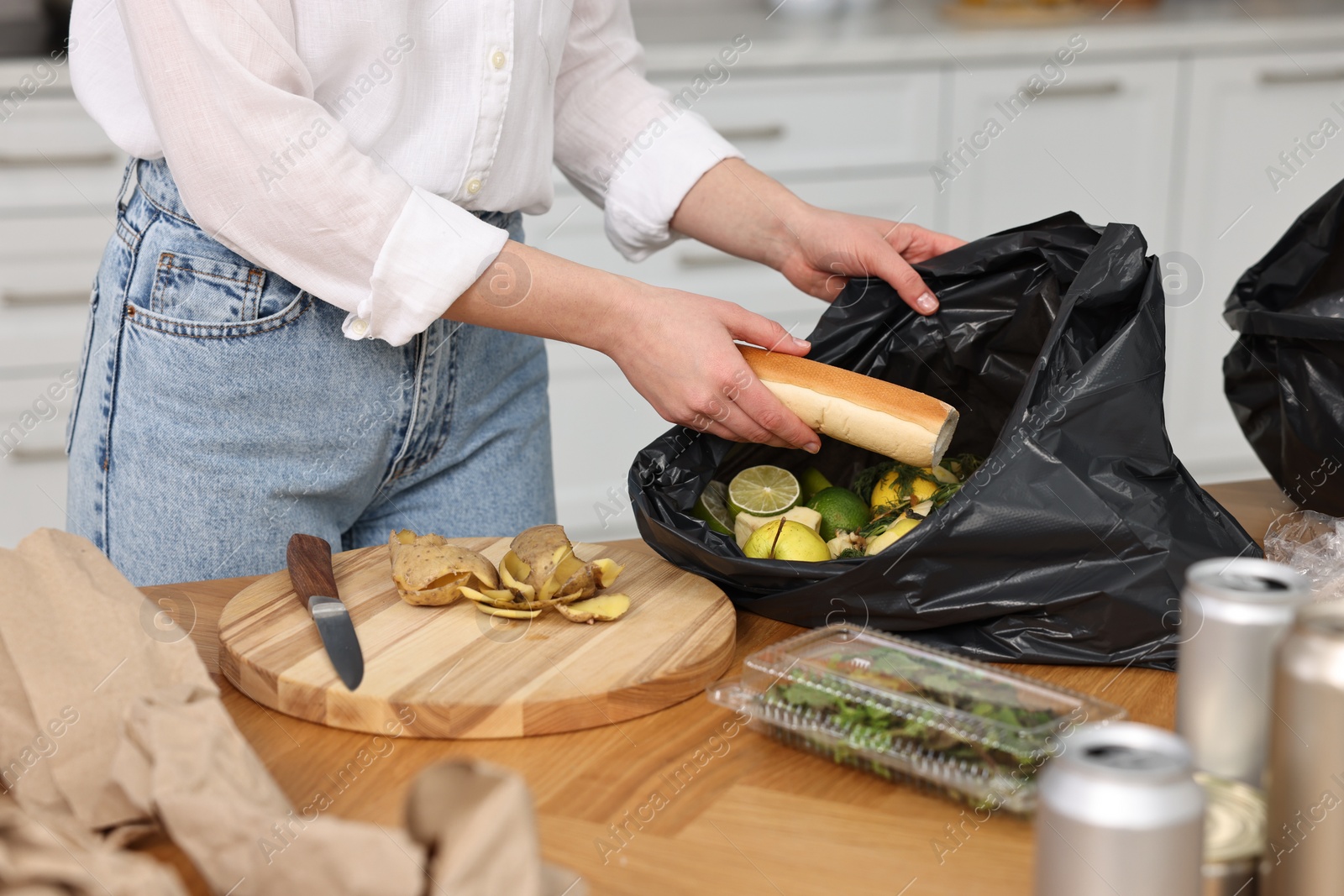 Photo of Garbage sorting. Woman putting food waste into plastic bag at wooden table indoors, closeup