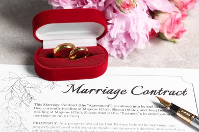 Photo of Marriage contract, fountain pen, golden wedding rings and flowers on grey table, closeup