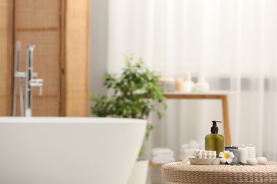 Spa products, burning candles and plumeria flower on wicker table in bathroom. Space for text