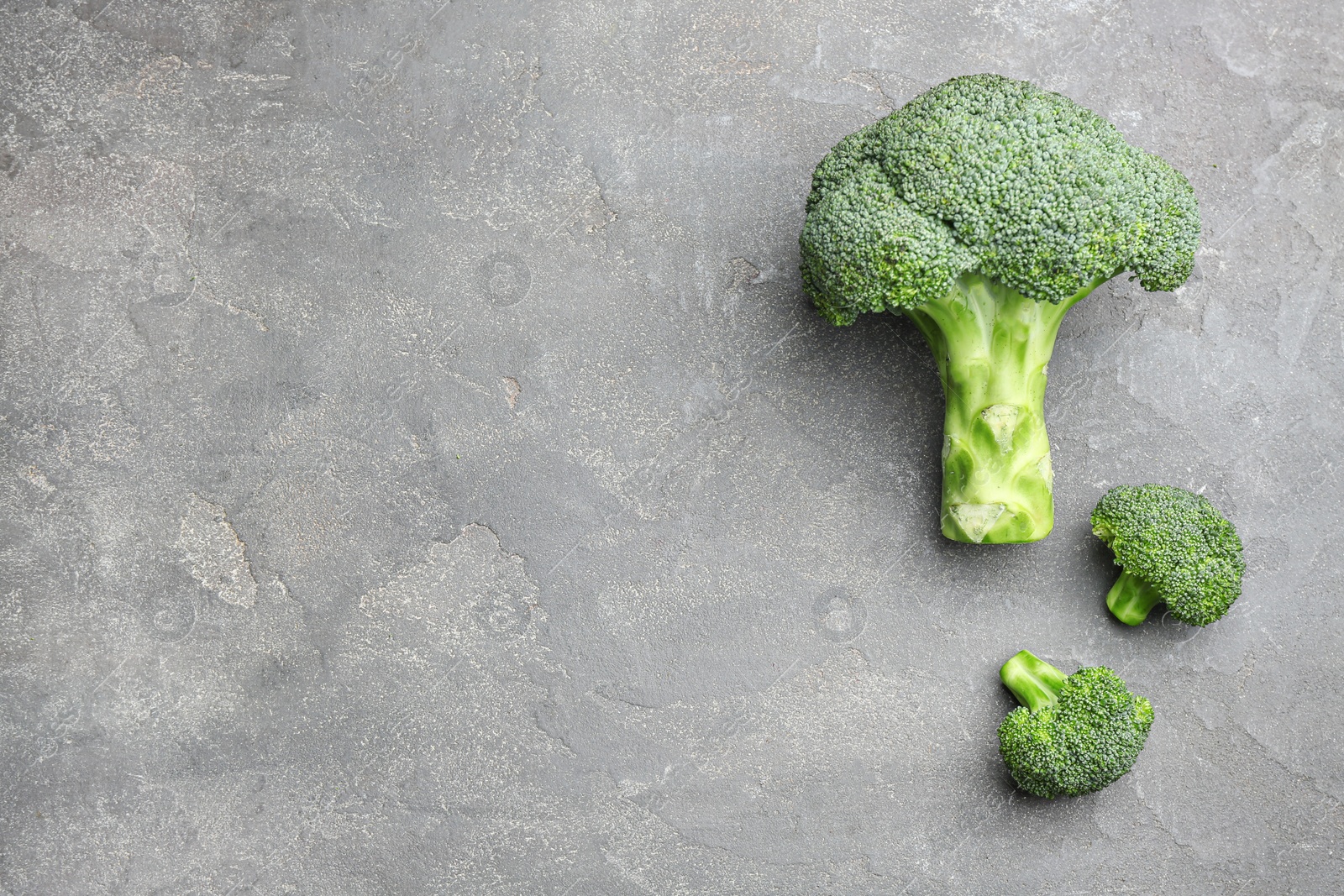 Photo of Flat lay composition of fresh green broccoli on grey stone table, space for text