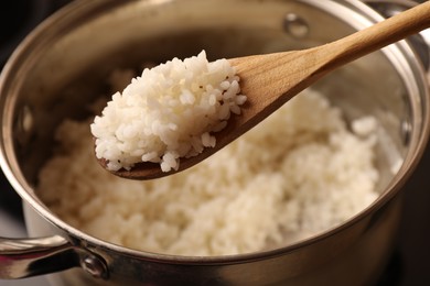 Photo of Wooden spoon with delicious rice over pot, closeup