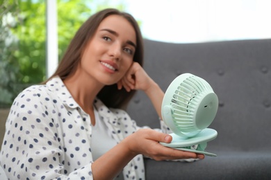 Woman enjoying air flow from portable fan at home. Summer heat