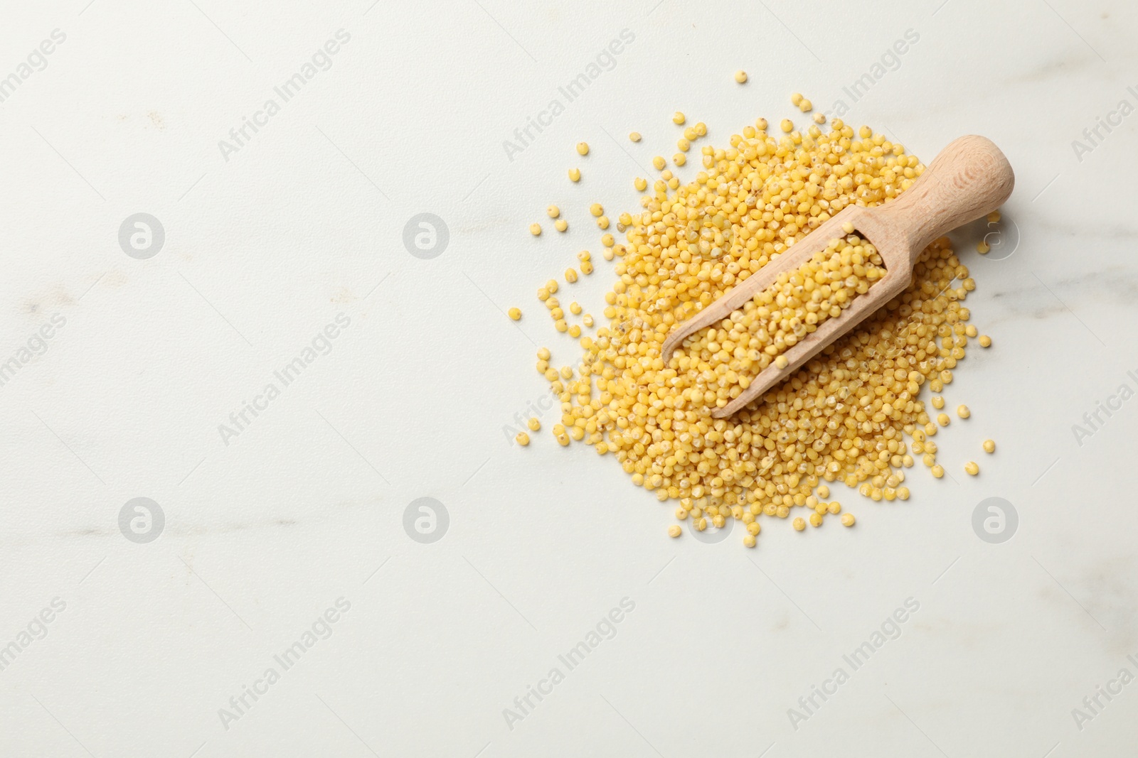 Photo of Scoop with millet groats on white marble table, top view. Space for text