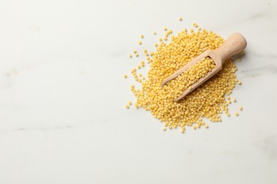 Photo of Scoop with millet groats on white marble table, top view. Space for text