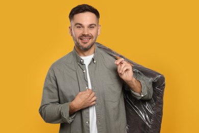 Photo of Man holding garment cover with clothes on yellow background. Dry-cleaning service