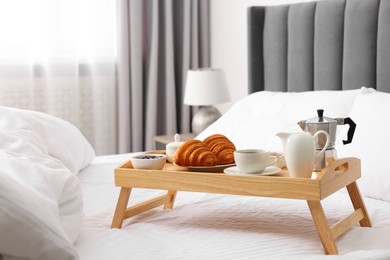 Photo of Wooden tray with tasty breakfast on bed at home