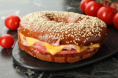 Photo of Delicious bagel with ham and cheese on dark marble table, closeup