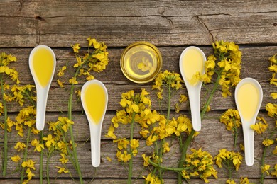 Photo of Rapeseed oil in bowl, gravy boats and beautiful yellow flowers on wooden table, flat lay