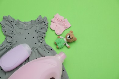Photo of Bottles of laundry detergents, baby clothes and toy bear on light green background, flat lay. Space for text