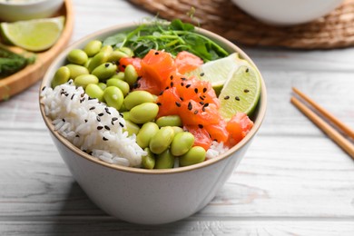 Photo of Delicious poke bowl with lime, fish and edamame beans on white wooden table, closeup