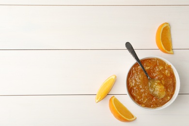 Delicious orange marmalade and fruit slices on white wooden table, flat lay. Space for text