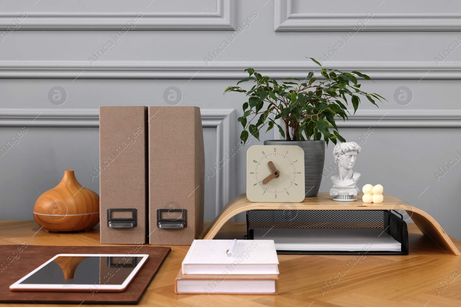 Photo of Stylish workplace with houseplant, tablet and stationery on wooden desk near grey wall at home