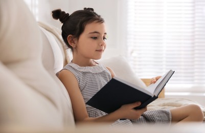 Photo of Little girl reading fairy tale in living room