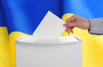 Image of Woman putting her vote into ballot box against national flag of Ukraine, closeup