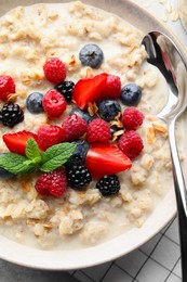 Bowl of oatmeal porridge served with berries on light grey table, top view