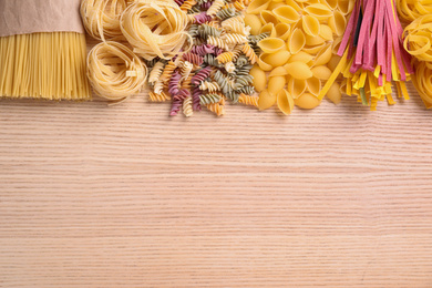 Different types of pasta on wooden table, flat lay. Space for text