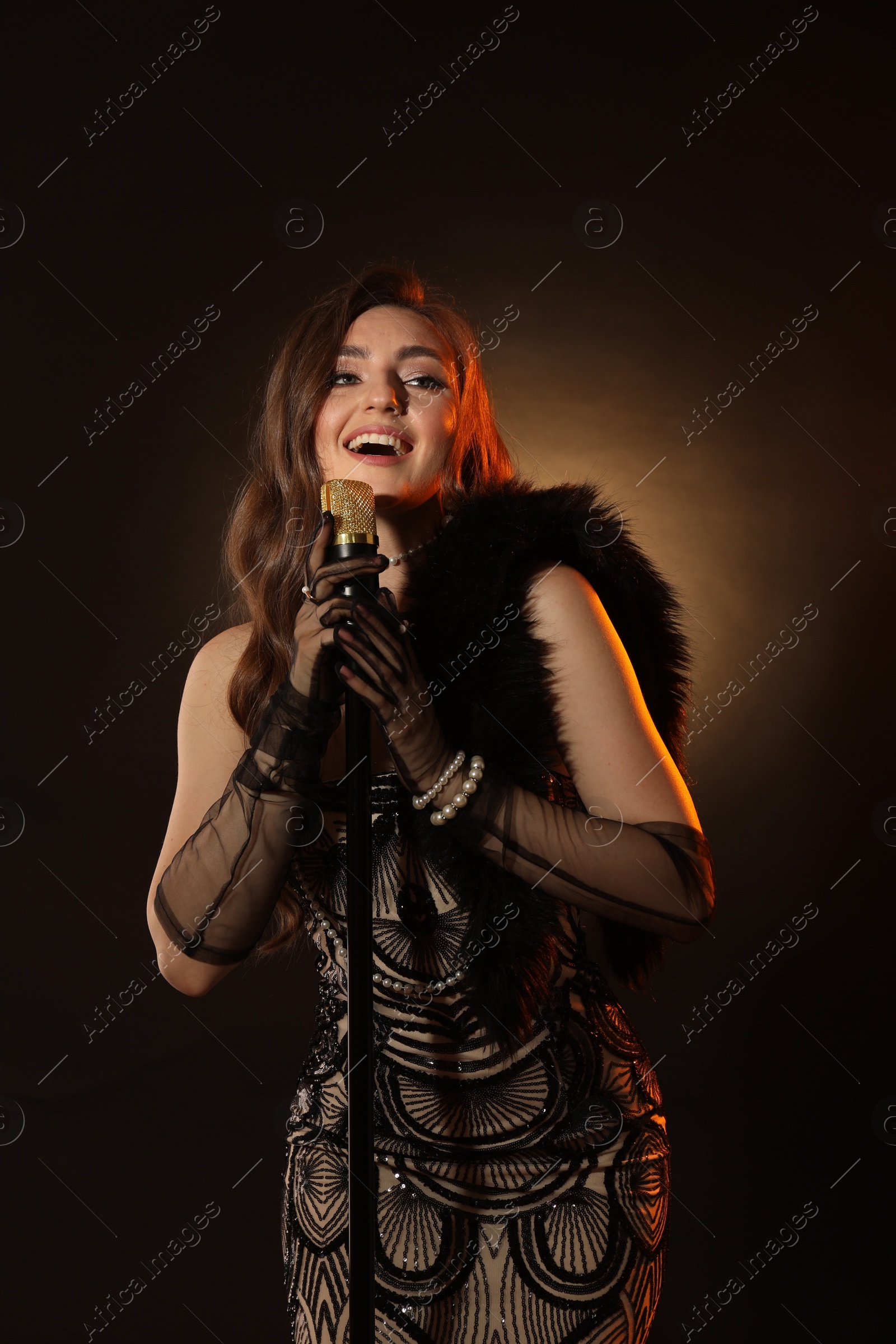 Photo of Beautiful young woman in stylish dress with microphone singing on dark background