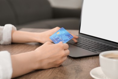 Woman with credit card using laptop for online shopping at wooden table indoors, closeup