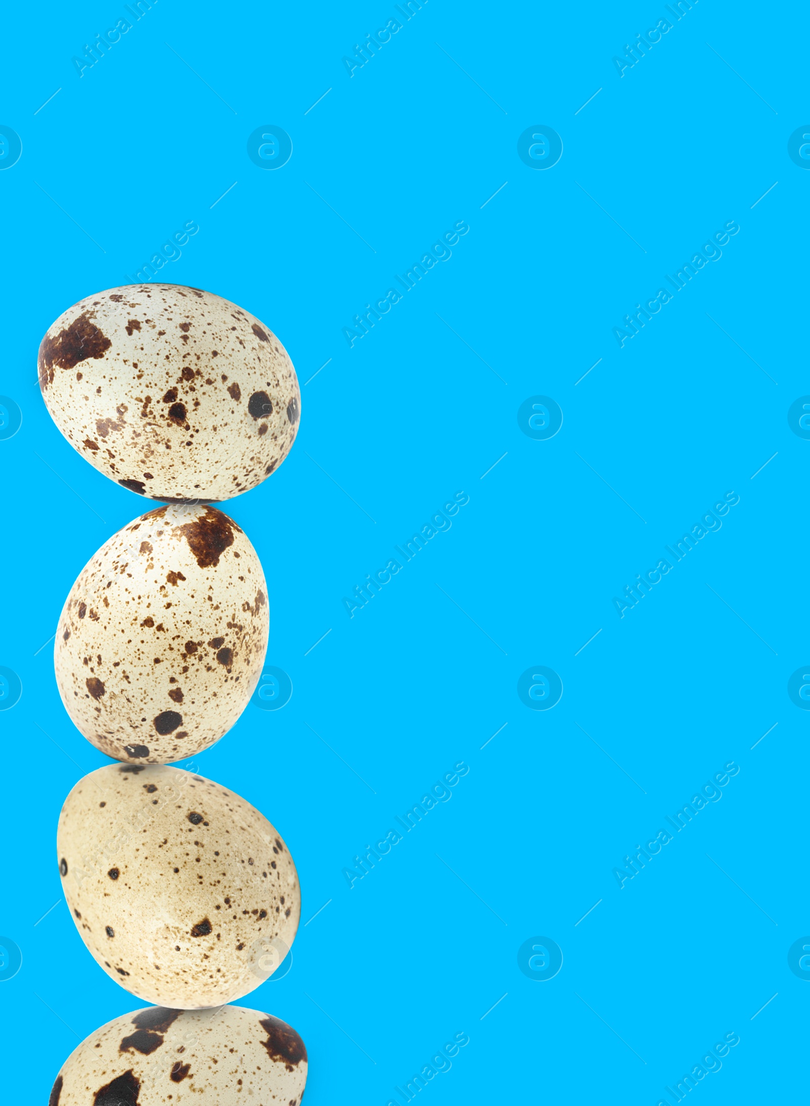 Image of Stacked speckled quail eggs on light blue background. Space for text