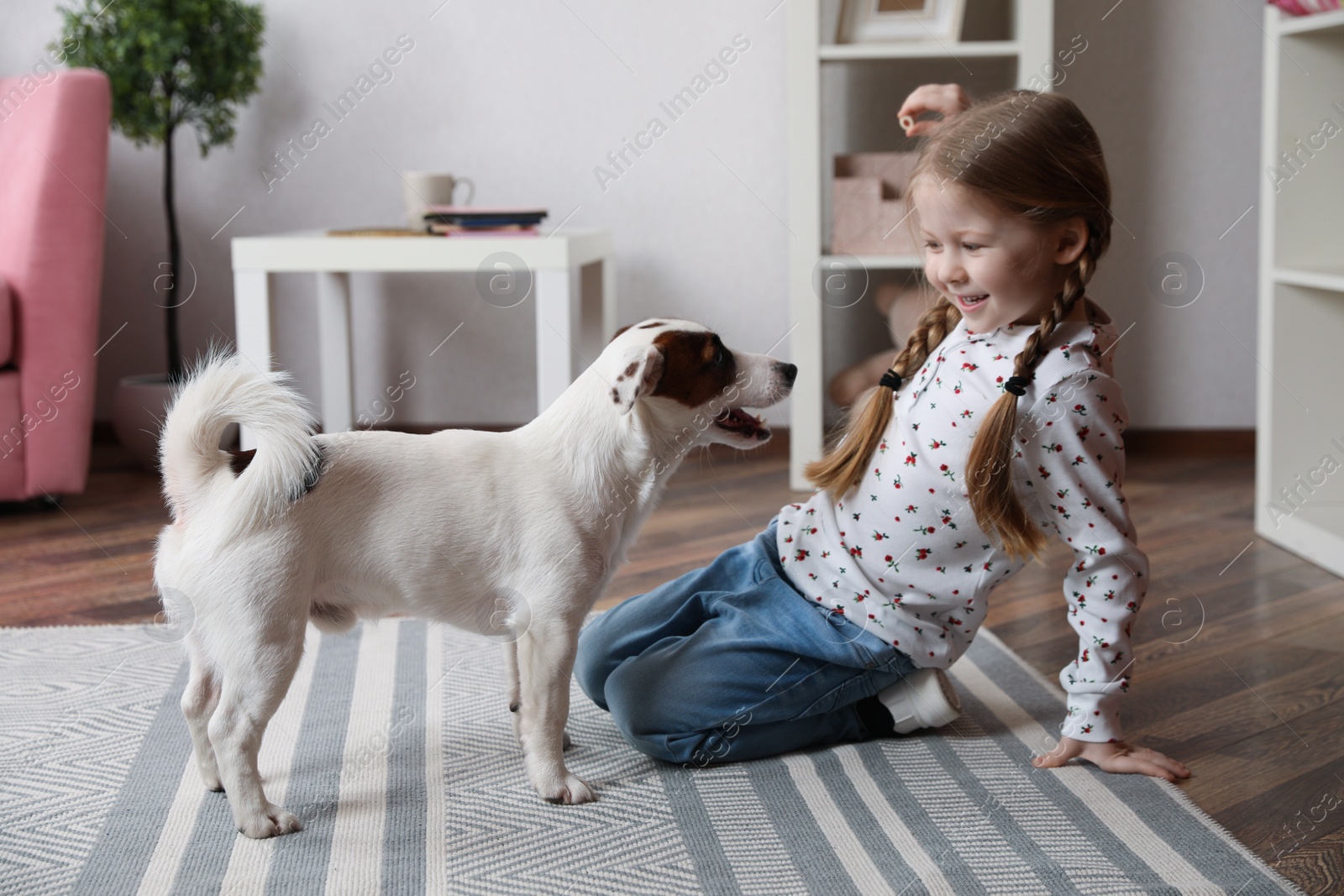 Photo of Cute little girl playing with her dog at home. Childhood pet