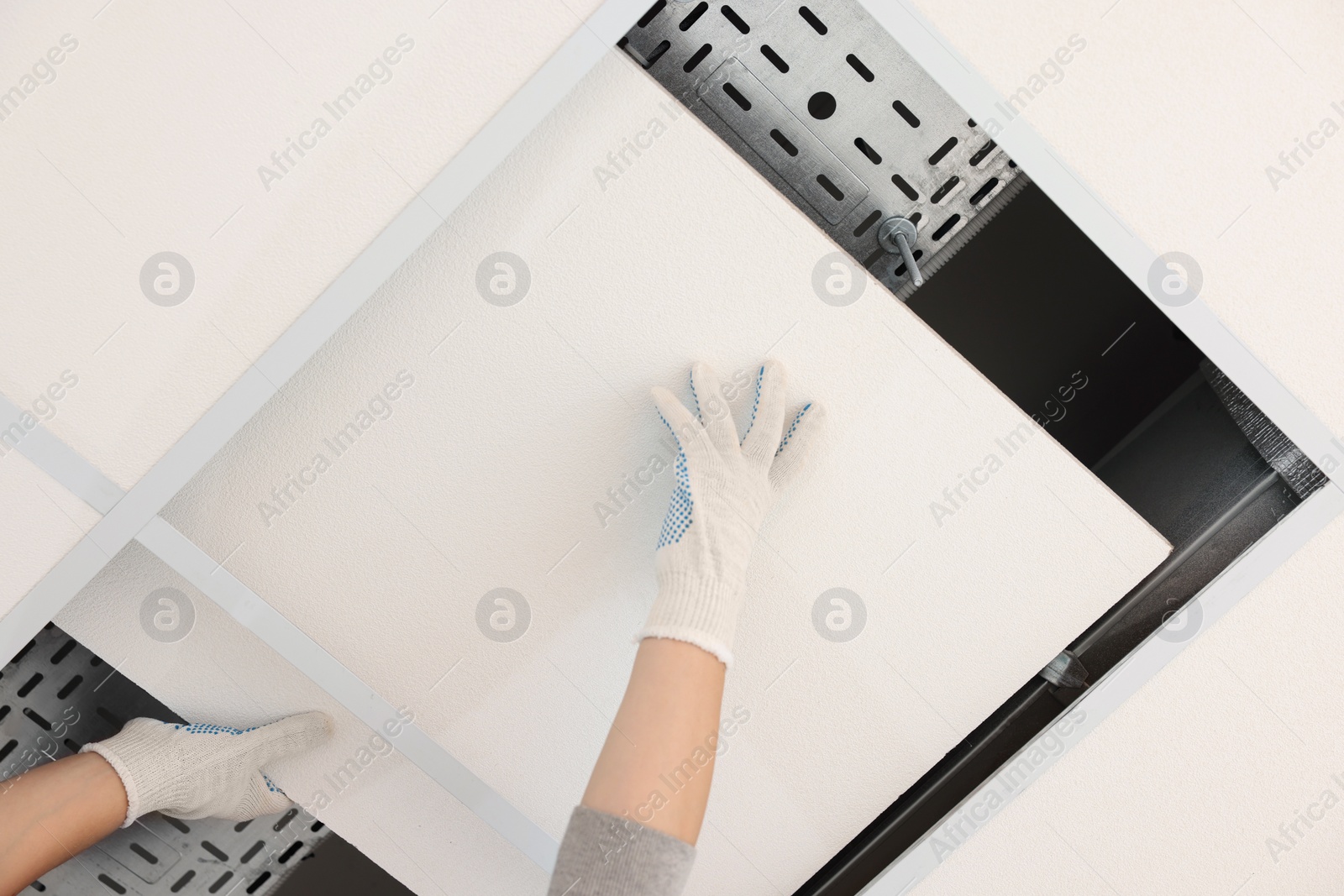 Photo of Suspended ceiling installation, bottom view. Builder working with PVC tile, closeup