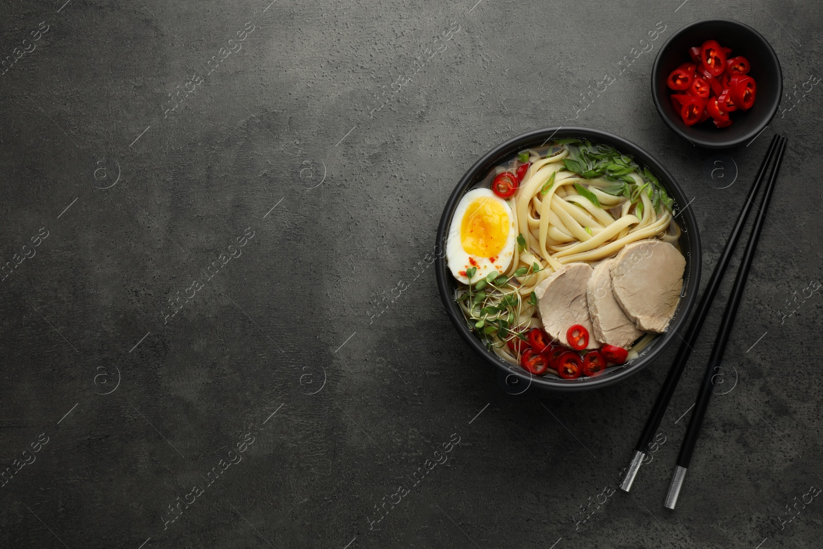 Photo of Delicious ramen with meat in bowl served on grey textured table, flat lay. Space for text. Noodle soup