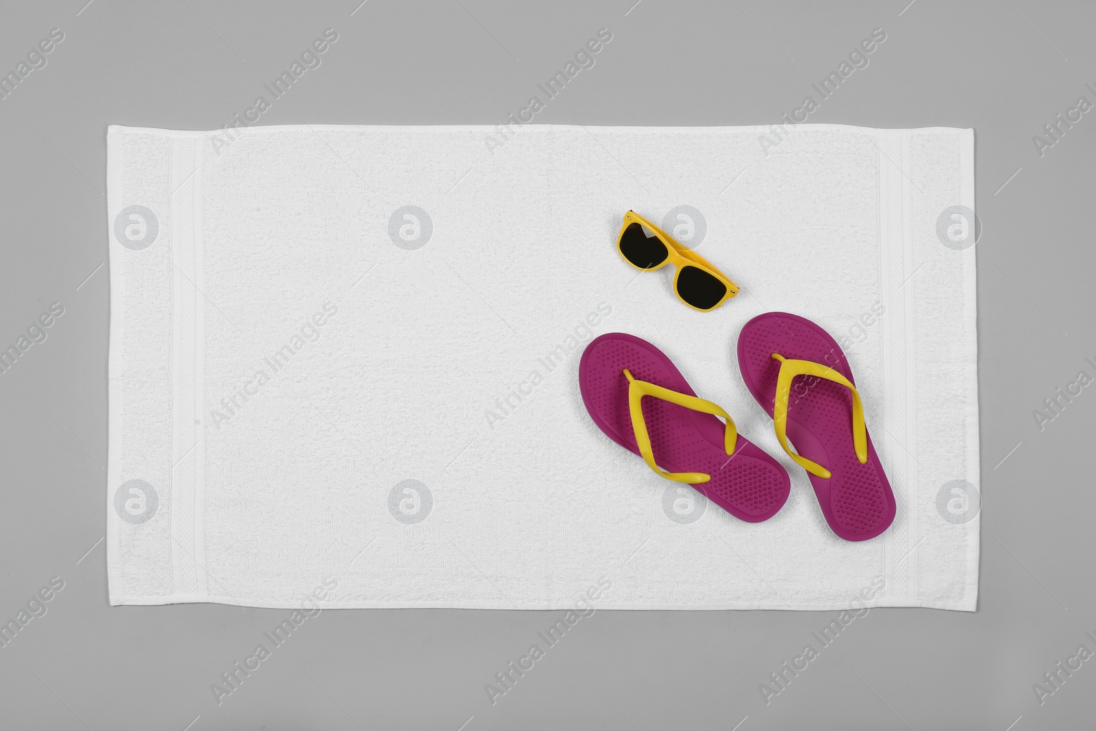 Photo of White beach towel with flip flops and sunglasses on light grey background, top view