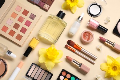 Photo of Flat lay composition with different makeup products and beautiful spring flowers on beige background