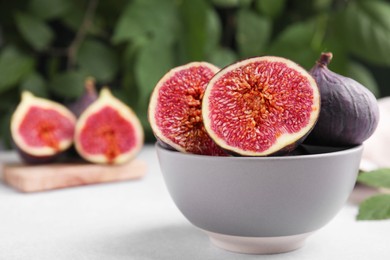 Bowl of tasty ripe figs on light table against blurred background, closeup