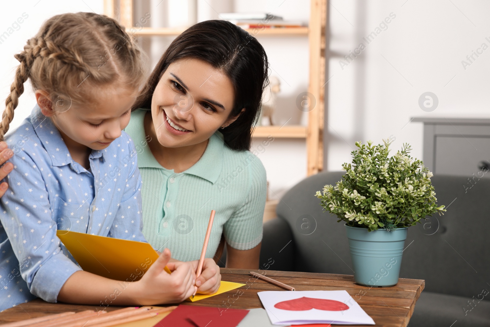 Photo of Cute little girl with her mother making beautiful greeting card at home