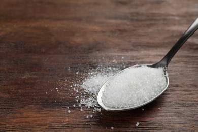 Photo of Spoon with granulated sugar on wooden table, closeup. Space for text