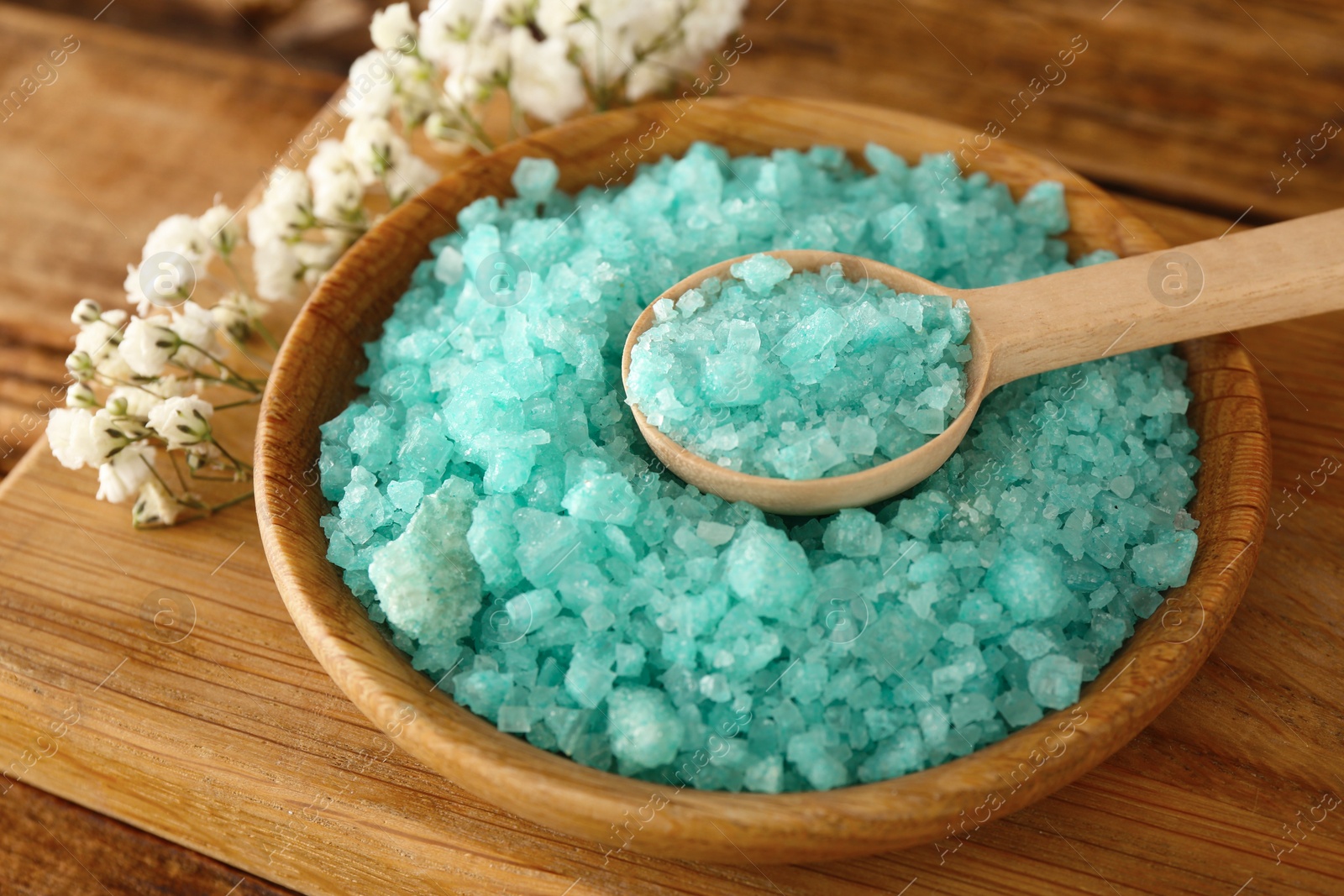 Photo of Turquoise sea salt and beautiful flowers on wooden table, closeup