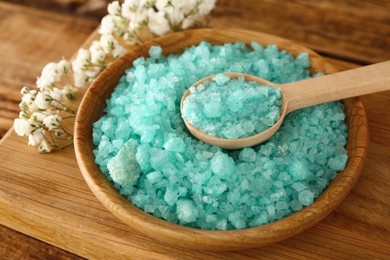 Photo of Turquoise sea salt and beautiful flowers on wooden table, closeup