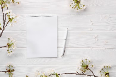 Guest list. Notebook, pen and spring tree branches with beautiful blossoms on white wooden background, flat lay. Space for text