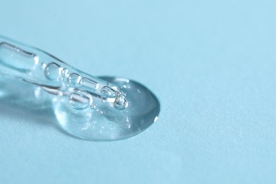 Photo of Glass pipette and transparent liquid on light blue background, closeup. Space for text