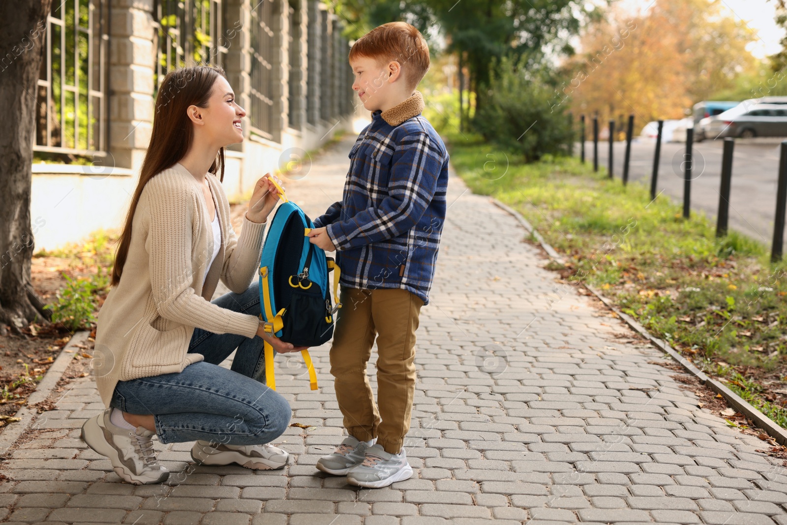 Photo of Young mom giving school backpack to her son outdoors