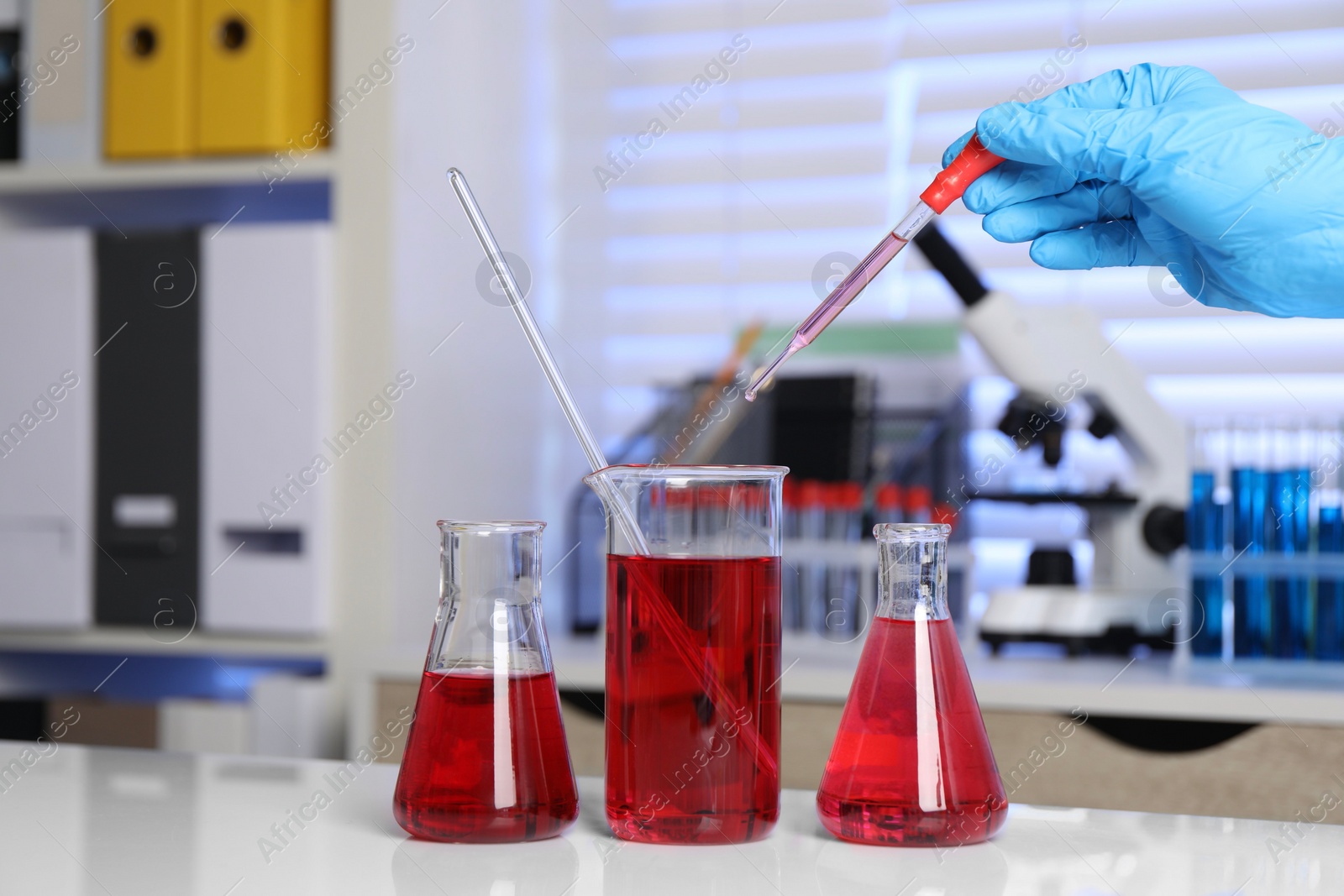 Photo of Laboratory analysis. Woman dripping red liquid into beaker on white table, closeup