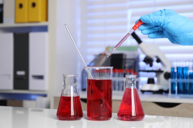 Laboratory analysis. Woman dripping red liquid into beaker on white table, closeup