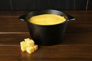 Fondue pot with melted cheese and pieces at wooden table