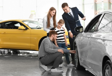 Photo of Young family choosing new car with salesman in salon