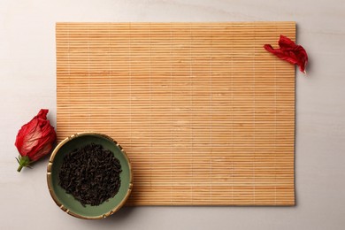 Photo of Bamboo mat, dry tea leaves and dried rose flower on beige table, flat lay. Space for text