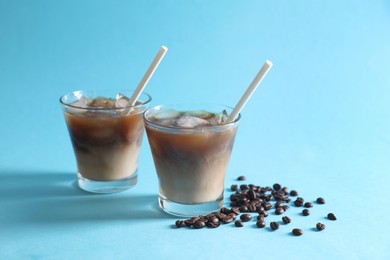 Refreshing iced coffee with milk in glasses and beans on light blue background