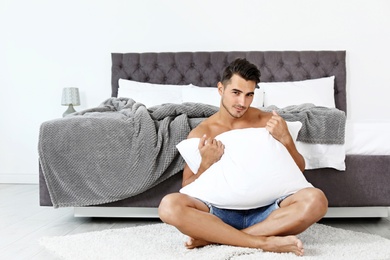 Sexy young man with soft pillow near bed at home