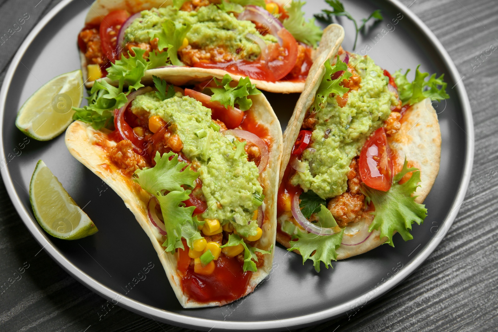 Photo of Delicious tacos with guacamole, meat and vegetables on wooden table, closeup
