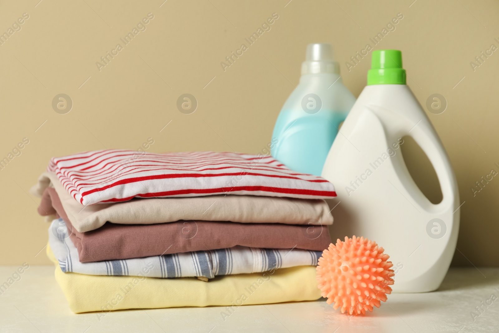 Photo of Orange dryer ball, laundry detergents and stacked clean clothes on white table